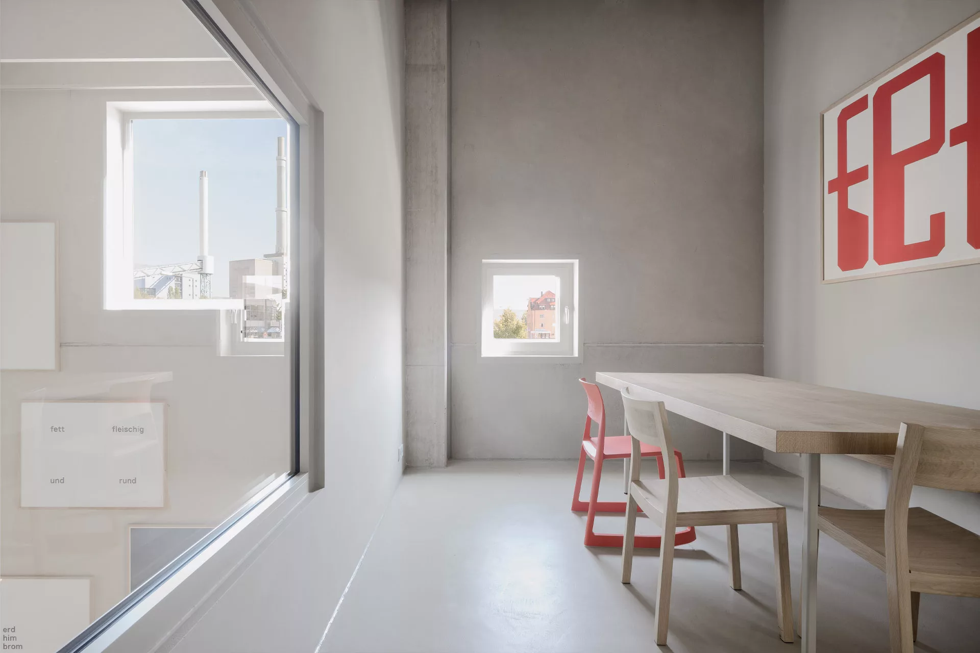 Minimalistisches Zimmer mit Holztisch, zwei Stühlen und rotem Kunstwerk an der Wand.